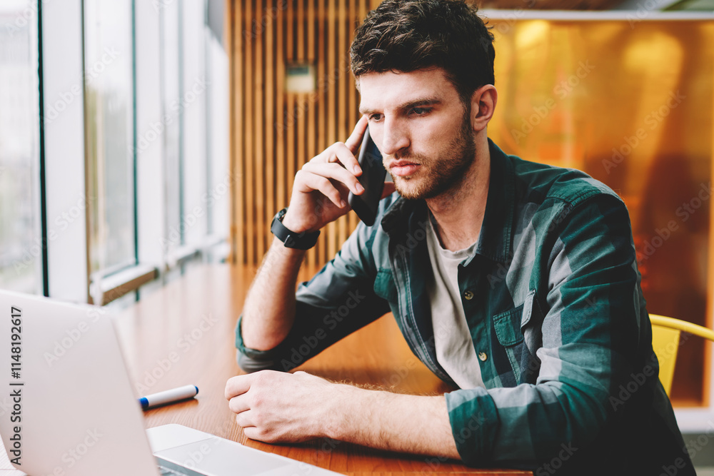 Aufkleber young handsome male designer having mobile conversation via application on smartphone while watching