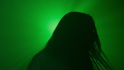 Woman silhouette dancing and moving head, clubbing at nightclub and raving against bright green colored spotlight, isolated on studio background.