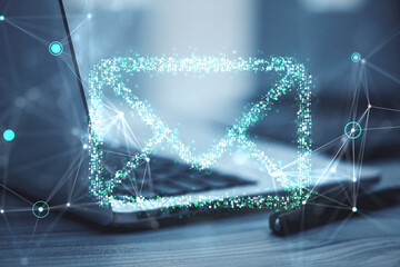 Digital email icon in holographic style over laptop on desk.