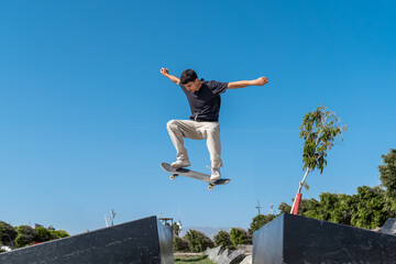 young skater wearing black tshirt jumping a pyramid ramp in Arinaga skate park. 