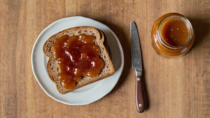 Top-View of Glass Jar with Fruit Jam and Peanut Butter, Homemade Whole Grain Wheat Bread Slices Spread with Sweet Jam, Rustic Wooden Kitchen Table, Healthy Snack or Sandwich