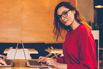 Portrait of clever female student looking at camera preparing for exams via laptop computer with serious colleague, young woman working on freelance in cafe interior concentrated on web development