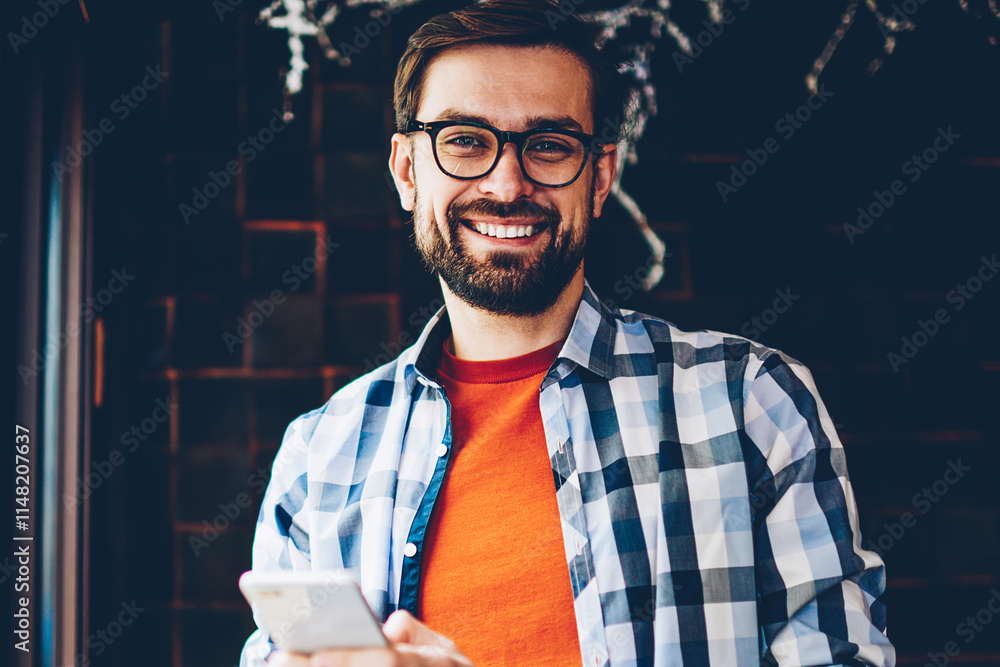 Poster portrait of happy bearded young man smiling at camera while typing text message on smartphone device