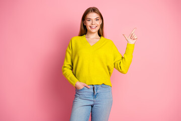 Young woman wearing bright yellow sweater pointing with her finger on a pink background