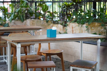 A minimalist wooden table and chairs in a cafe with a blue tissue holder in the middle without anyone sitting on it