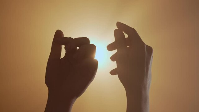 Close up shot of female hands silhouette moving fingers against bright golden colored spotlight, isolated on dark studio background.