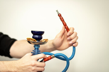 Hands holding a compact hookah with a purple glass base, blue hose, and dried citrus in the bowl....