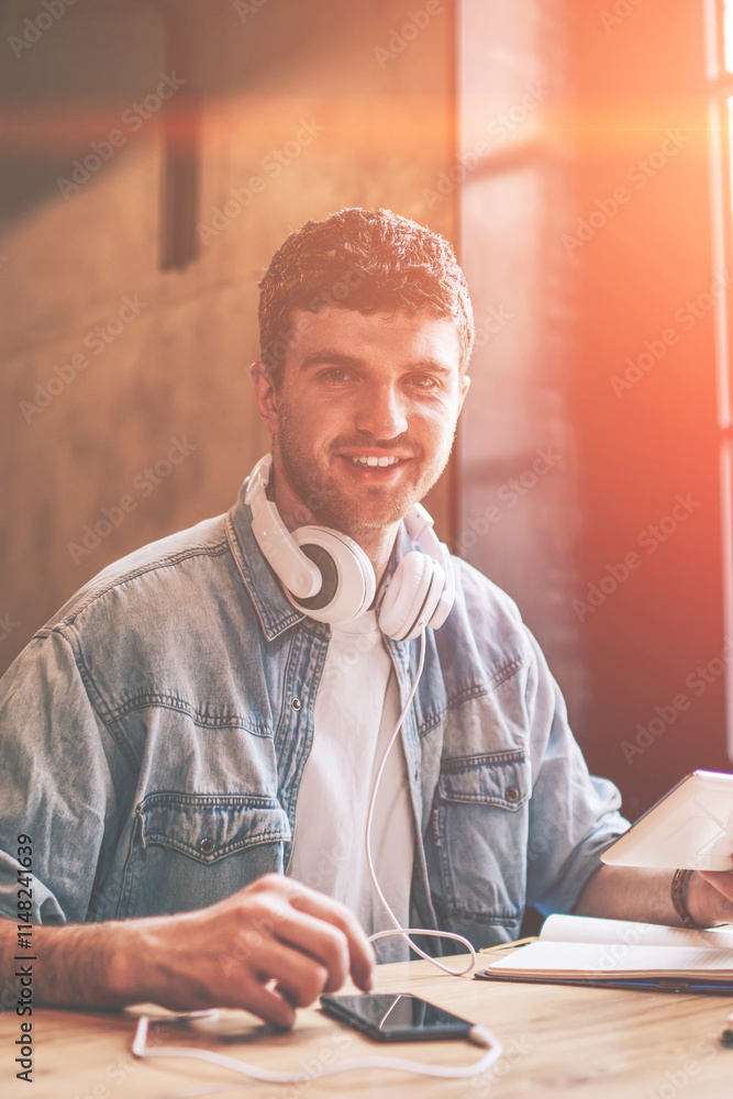 Poster portrait of cheerful hipster guy with touch pad in hand looking at camera while installing media app