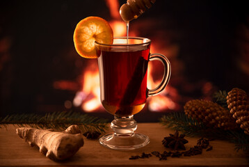 A glass of mulled wine on a wooden table in front of a burning fireplace. Hot mulled wine with a...