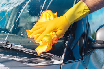 Person cleaning car windshield with yellow gloves and cloth on a bright sunny day