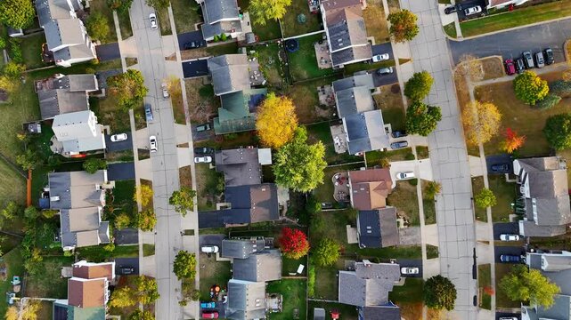 Aerial View of Suburban Neighborhood in Autumn. Overhead view of a quiet suburban neighborhood with tree-lined streets, colorful autumn foliage, and parked cars in driveways.