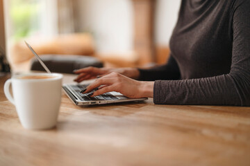 Woman working on laptop at wooden table with coffee cup in cozy environment during daytime
