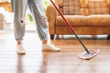 Woman cleaning wooden floor with mop in cozy living room during daytime