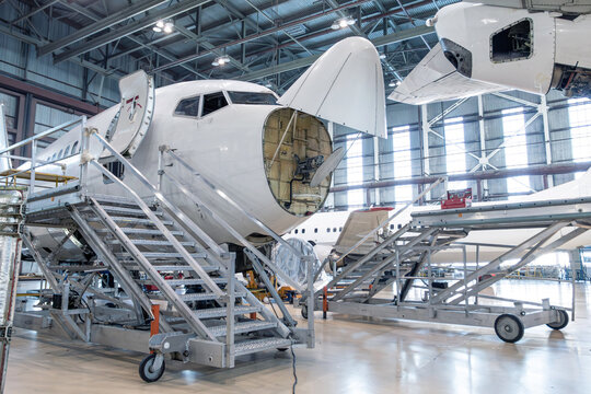 Front view of the white passenger plane under maintenance in the airplane hangar. The aircraft has opened weather radar. Checking mechanical systems for flight operations