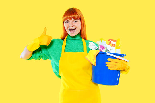 Cheerful woman holds cleaning supplies and shows thumbs up against bright yellow background
