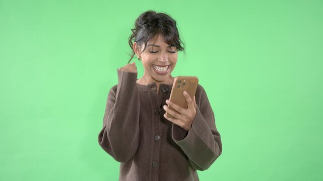 Young woman enjoy news on mobile phone while standing against a green background