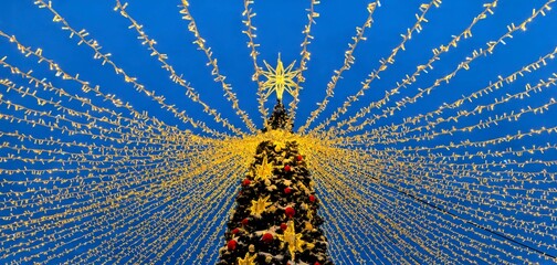 Christmas tree outside, decorated with lights, stars and garlands against the blue sky - horizontal photo, winter decor in Moscow parks