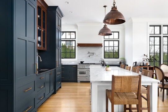 A modern farmhouse kitchen with blue and wood cabinets, brushed bronze pendant lights hanging over a large white island, and a blue and white tiled backsplash. No brands or labels.