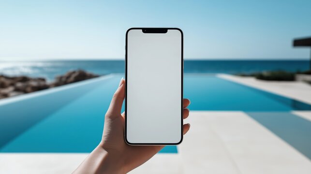 A hand holds a blank screen smartphone in front of a stunning poolside view, perfectly capturing a relaxing summer moment - Powered by Adobe