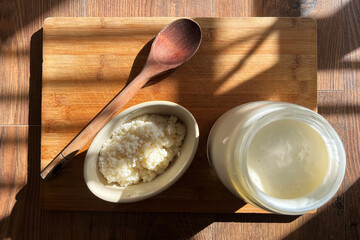 Milk kefir strained into a container with strained kefir grains ready for making more fresh kefir. Set on a wooden board with the morning sun casting dramatic light over them.