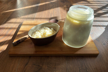 Milk kefir strained into a container with strained kefir grains ready for making more fresh kefir. Set on a wooden board with the morning sun casting dramatic light over them.