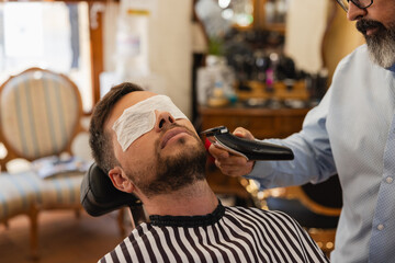 barber shop concept and people - Barber trims man's beard with electric clippers