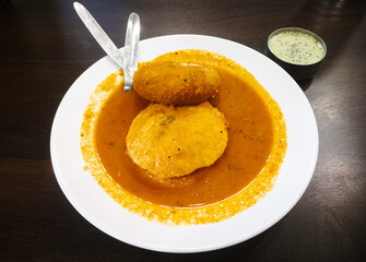 Delicious authentic Idli Vada dipped in sambar with coconut chutney served on a white plate on a...