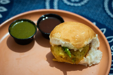 Delicious mumbai vada pav with green chutney and tamarind chutney on a plate.