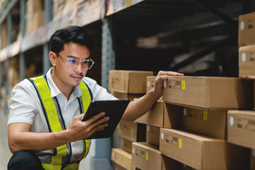 A man in a yellow vest is looking at a tablet while standing in a warehouse. He is wearing glasses and he is focused on the tablet