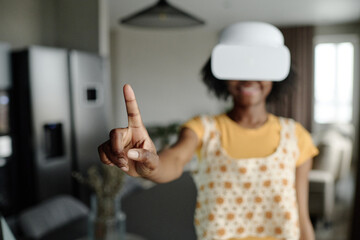 Woman smiling widely and gesticulating while using VR headset, focus on female index finger