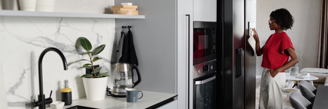 Website banner with African American housewife standing in front of smart fridge and setting it in modern kitchen - Powered by Adobe