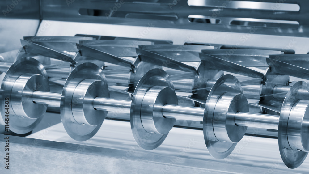 Poster A machine with a row of metal gears. The gears are silver and are lined up. The machine is in a factory