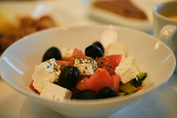 A simple lunch in a Greek cafe. The traditional salad with vegetables and cheese includes tomatoes, cucumbers, olives, feta cheese and olive oil with spices. Close up view.