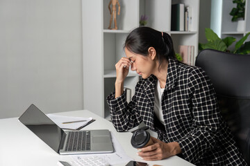 Stressed Young Accountant Working at Desk with Laptop and Coffee in Modern Office Environment