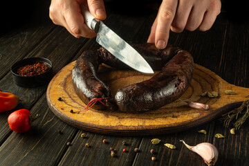 A chef cuts blood sausage with a knife on a wooden breakfast cutting board. Close-up of the cook...