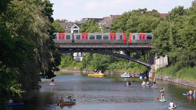 Subway Train Crossing Bridge Over Alster River with Paddleboarders and Boaters on a Hot Summer Day in Hamburg