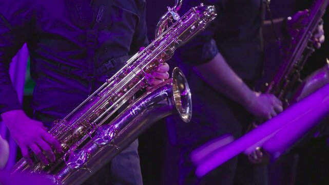 A musician playing the baritone saxophone with a tenor sax player in the bakcground and all are dressed in black during a live performance