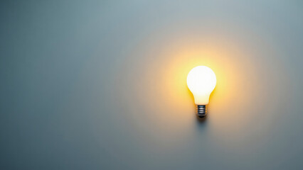 A glowing yellow light bulb illuminated against a soft gray wall, perfect for home decor.