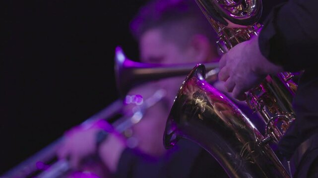 A musician playing the baritone saxophone with trumpet players and all are dressed in black during a live performance