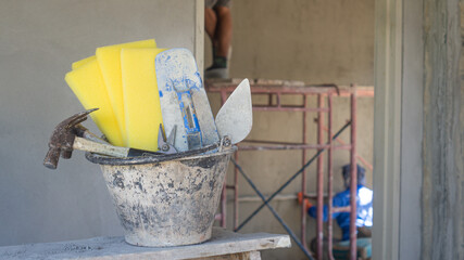 Builders' tools are put together in a bucket placed on a wooden table. On the background of the working atmosphere of professional workers and technicians. Copy space