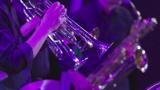 Two trumpet players with a baritone saxophone player all dressed in black during a live jazz concert illuminated by purple stage lights
