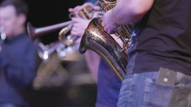 A practice session of a brass group, but the baritone saxophone has a solo and he is wearing jeans and a black shirt