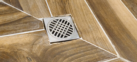 Water drain in the bathroom and tiles with wood texture. 
Bathroom sewer close-up