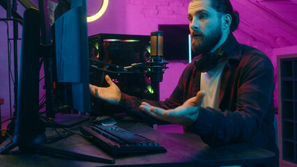 Caucasian gamer man addict puzzled influencer streaming play videogame blog computer screen surprise confused male guy blogger removing headphones shock scam losing game cheat e-sport problem at home