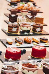 A table with many desserts including cakes and donuts. There are also some containers with different types of desserts