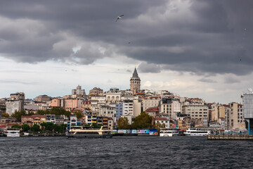 Iconic Galata Tower at sunset in Istanbul, Turkey. Distinctive conical shape and golden spire, stands tall against dramatic sky with fluffy clouds. Bustling cityscape with rooftops and buildings