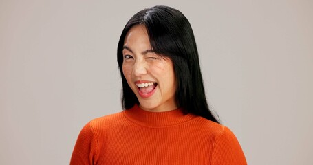Asian woman, wink and portrait in studio with smile, playful or flirting with emoji by background. Girl, person and model with funny eye sign, icon and happy with laughing for secret symbol in Taiwan