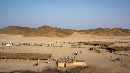 Desert Adventure: A Scenic Gathering at the Camp with White Vehicles and People Amidst Sandy Dunes and Rocky Hills Under the Clear Blue Sky, Capturing the Essence of Exploration and Tranquility