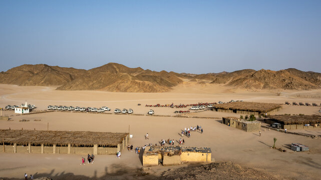Desert Adventure: A Scenic Gathering at the Camp with White Vehicles and People Amidst Sandy Dunes and Rocky Hills Under the Clear Blue Sky, Capturing the Essence of Exploration and Tranquility
