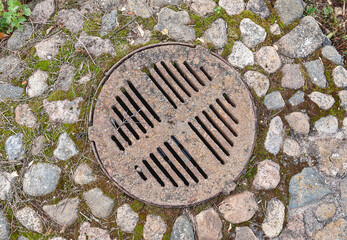 Rustic manhole cover surrounded by moss and cobblestones